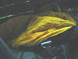 Der nasse Schlafsack im Hochsitz. Zu sehen ist das gelbe Innenfutter des Schlafsackes, der bis -10° C noch gut vor der klirrenden Kälte schützt. Daneben, an dem Wanderrucksack befestigt, eine doppelwandige Edelstahltasse.